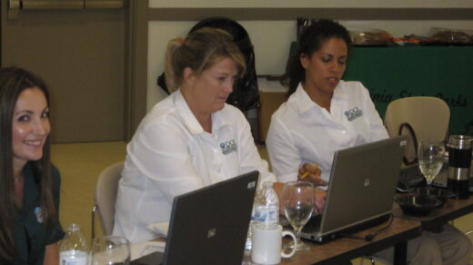 Women in white shirts working on laptops at a conference table